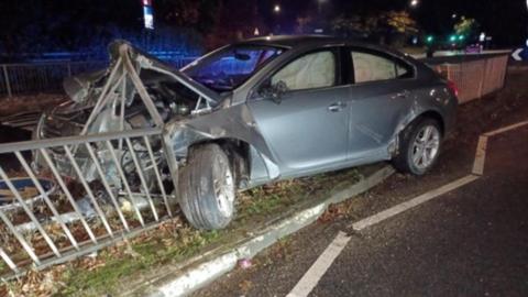 A car that has the front damaged and crushed as it has crashed into railings