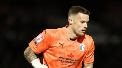 Barrow goalkeeper Paul Farman, wearing an orange kit, about to take a goal kick