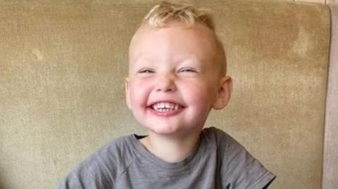 The late three-year-old Albie Speakman who has blond hair and a beaming smile wearing a grey t-shirt 