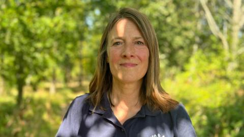 Rachel Paget smiling for the camera. She is stood outdoors in a wooded area.