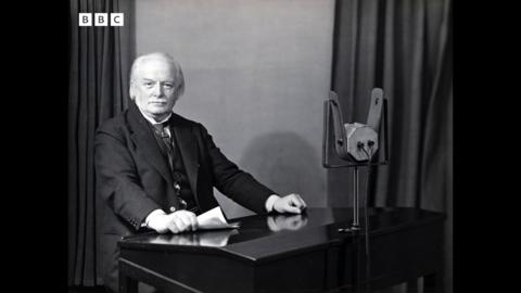 David Lloyd George sits in front of a microphone