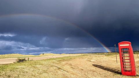 Very dark skies and a rainbow with a red phone box in the foreground