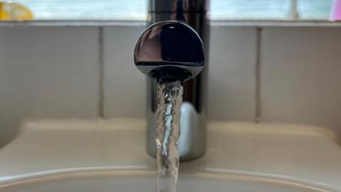 A close-up of a tap turned on with water spilling out of it.