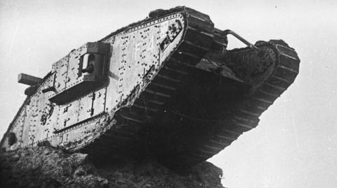 Black and white photo of a Mark IV tank, which stands on the edge of a precipice with half of the vehicle hanging over the edge in mid-air.