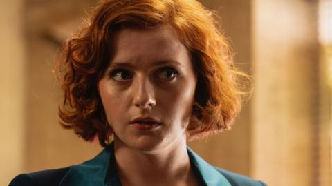 A woman with red hair and a blue jacket looks right out of frame.