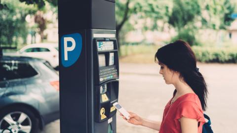 A young woman in a red top, using her phone next to a parking meter