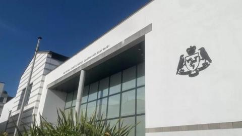 The exterior of the Courthouse, a grand white building with large windows,.