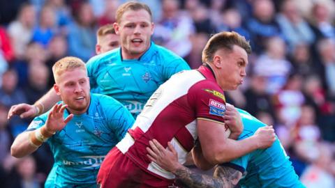 Wigan's Harvie Hill is tackled by three Huddersfield players  