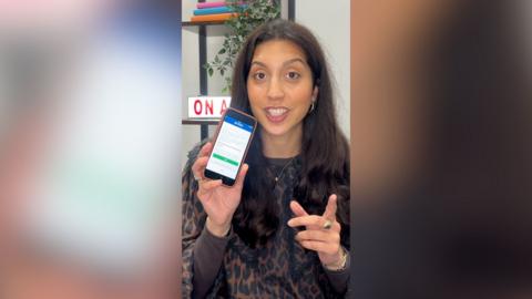 A woman with shoulder-length hair holds up a phone showing the new results app.