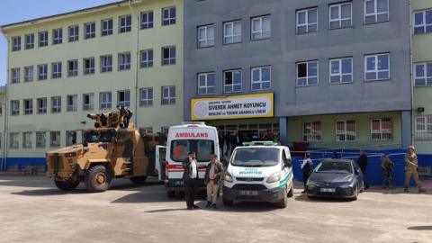 An armoured police vehicle, an ambulance and a vehicle for transporting bodies are parked at the entrance of a school 