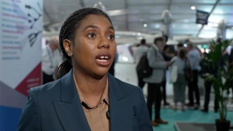 Kemi Badenoch in a tan shirt with a blue blazer