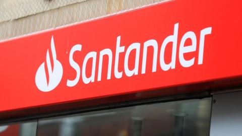 Close-up of a Santander bank branch sign. The logo and text are white and the background is red.