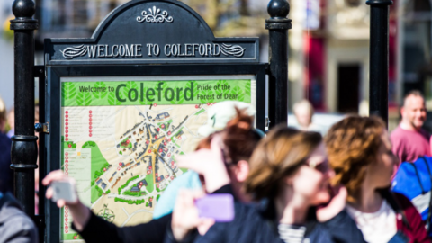 A wrought iron signboard says Welcome to Coleford in white letters, above a colourful map of the town which highlights many of the attractions to be found in the town centre.