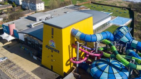 An aerial shot of the Alpamare waterpark featuring a yellow main building, with blue, green and pink slides emerging.