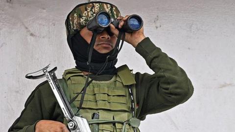 An Indian paramilitary personnel conducts surveillance using binoculars as he stands atop a commercial building in Srinagar 