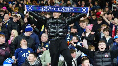 Fans celebrate in the Scotland stands, including a man dressed in black who holds up a Scotland scarf