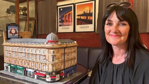 Karen, a woman in her 50s with dark brown hair and glasses on her head, sitting next to the model of Union Corner.