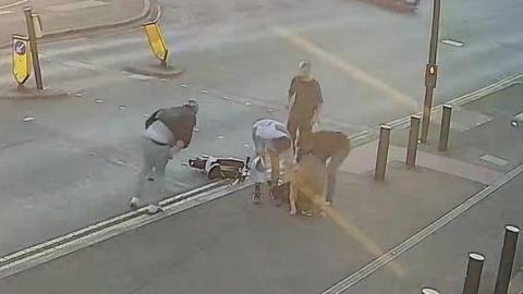 A group of people surround a woman who has been knocked over by an e-bike