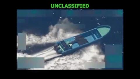 An aerial surveillance photo shows a long boat speeding through the water with wake and whie water all around it. Above the picture, it says "unclassified".