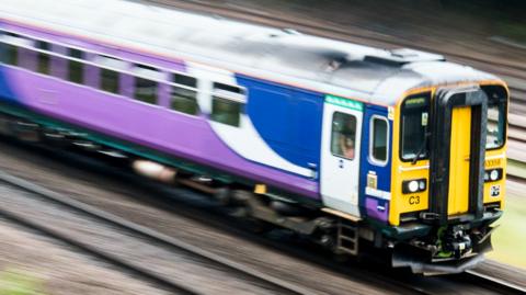 A train in purple and blue Northern Trains livery is pictured in motion on train tracks 