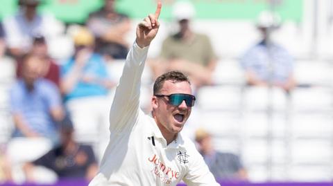 Liam Patterson-White celebrates taking a wicket by raising his right hand with his index finger pointing towards the sky.