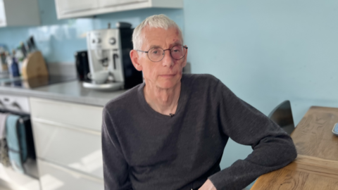 Paul Gosling sits at a wooden table in a blue kitchen