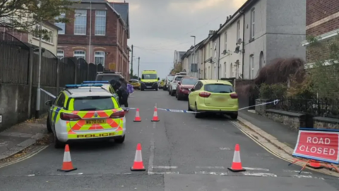 A road closure in place at the scene. A police vehicle and ambulance are parked on the road. A cordon is in place. 