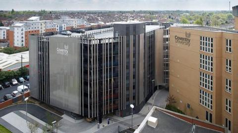 Coventry University buildings seen in an aerial image showing the paved area outside and a car park behind them.