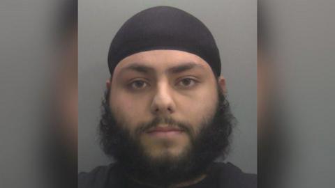 A police custody shot of a bearded man 