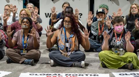 Climate activists at COP29 in Baku holding up hands with 'pay up' written on them.