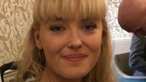 A woman with long blonde hair is smiling while looking at the camera.