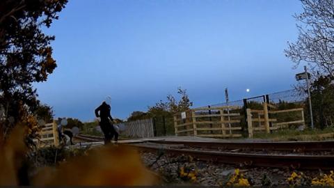 Dealbh bho Network Rail a' sealltainn dhaoine òga air an loidhne rèile