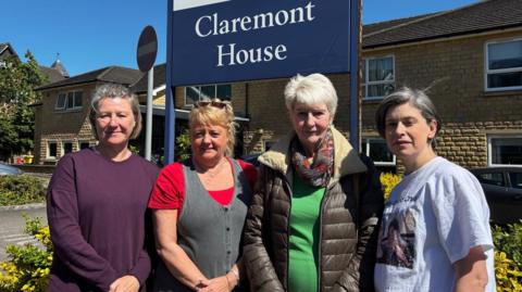 Four women stood in front of a red brick, two-storey care home. There is a blue sign indicating it is Claremont House.
