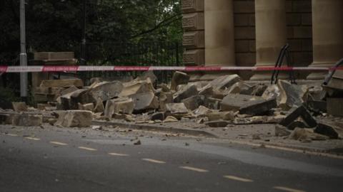 Big stones lying on road in front of Victorian building with red and white cordon in the foreground
