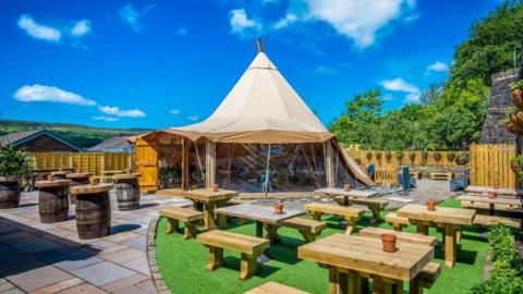 A photo of the outdoor space, including a large tipi, outdoor benches, pergola and patio at the Eagle and Child pub in Ramsbottom.