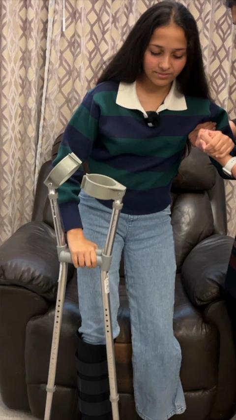 Kiara is attempting to stand up using her crutches and a person's hand as support.