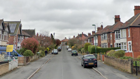 A street view from the centre of the road in Costock Avenue. There are rows of houses either side with cars parked on both sides of the road. 