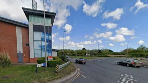 Roads leading to and off a roundabout with a building to the left.