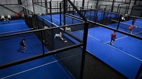 Four people play padel on blue and black indoor courts
