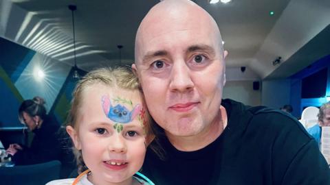Chris Capstick is sitting next to his daughter Isabella in a restaurant. They are smiling at the camera for this posed photograph. 