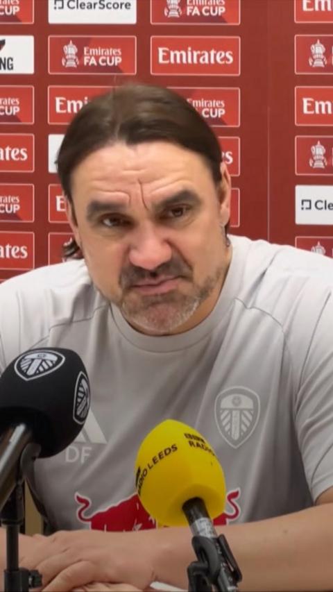 A man with short brown hair and stubble speaks in front of microphones at a press conference