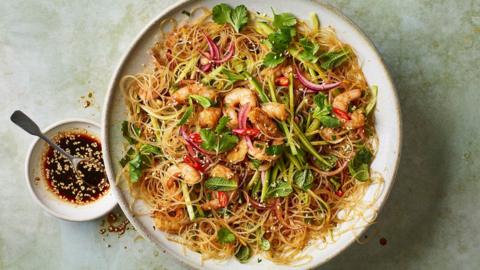 A white plate of noodles and prawns on a mottled green surface
