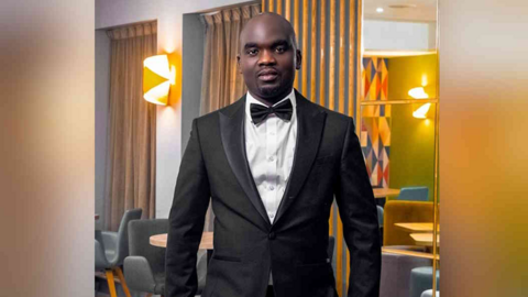 Legton Zulu standing in a black suit and bow-tie with a white shirt. He is looking directly at the camera and smiling.