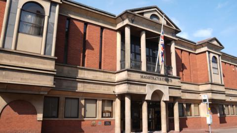 A view of Leicester Magistrates Court, a red brick building with beige stone features and a Union Jack outside