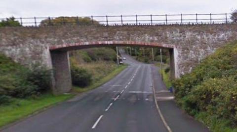 A stone bridge over a road with is stretching downhill into the distance.