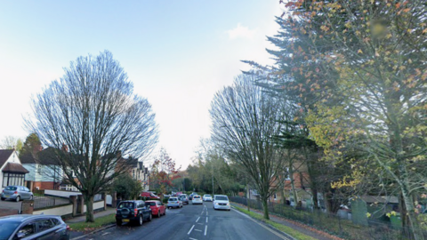 St Helen's Road in Hastings has houses on one side of the road and railings running along the other side. There are cars parked near the houses, and vehicles driving on the road.