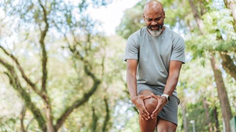 Someone outside in shorts and a t-shirt grasping their knee.