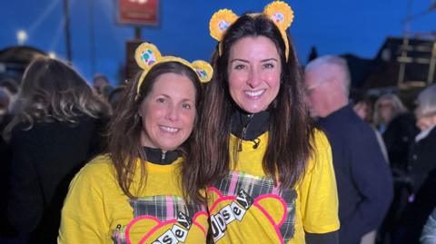 Lindsey Burrow and Amy Garcia, who are both smiling looking at the camera, wearing yellow T-shirts and Pudsey bear ear headbands.