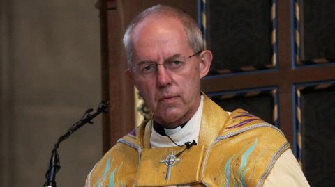 Archbishop Justin Welby at a pulpit in yellow robes.