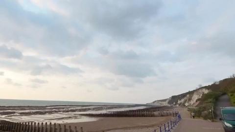 Eastbourne seafront is seen with cliffs in the background and the tide leaving pools on the beach